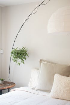 Bright minimalist bedroom with cozy pillows and hanging houseplants, ideal for relaxation.